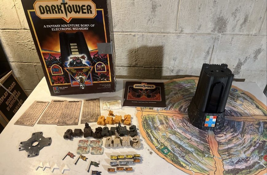 Vintage Dark Tower board game with box, electronic tower, map, game pieces, and cards spread out on a table, against a concrete wall background