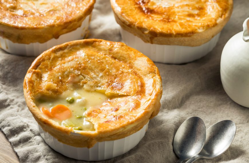 Mini chicken pot pies with golden crusts in white ramekins, creamy vegetable filling visible in one, spoon nearby