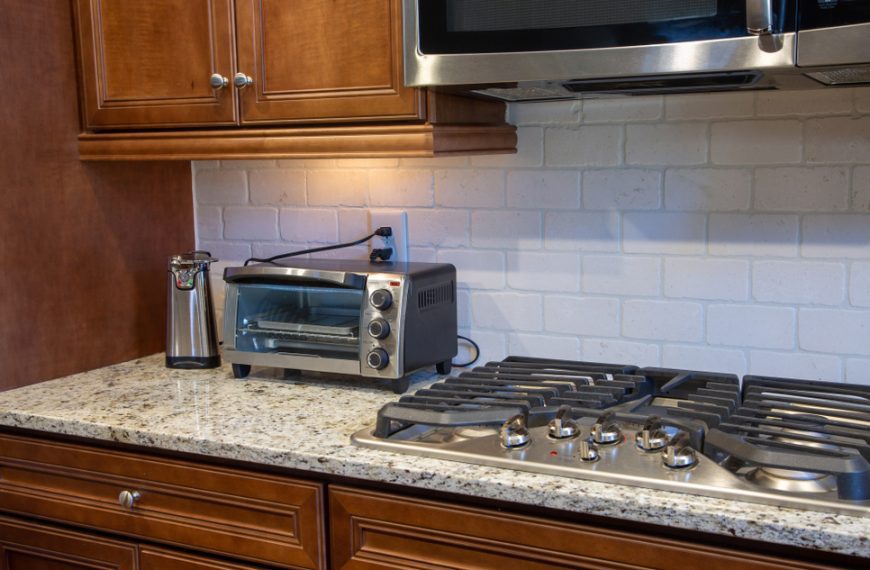Modern kitchen counter with a toaster oven, gas stove, toaster, and microwave above granite countertops