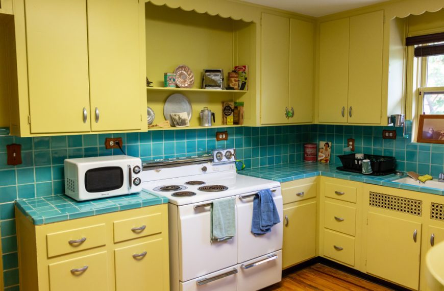 Retro kitchen with yellow cabinets, turquoise tile backsplash, vintage white stove, microwave, decorative plates, wood flooring