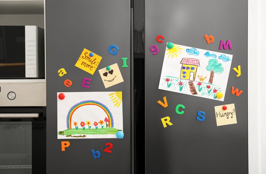 Children’s drawings on a refrigerator door, colorful alphabet magnets scattered around, rainbow and house artwork pinned with red magnets