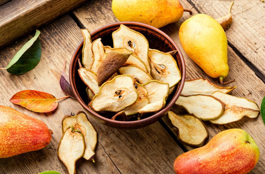 Bowl of dried pear slices, arranged on a wooden surface, surrounded by whole fresh pears in yellow and red hues, scattered green leaves, rustic and natural presentation, healthy snack setting