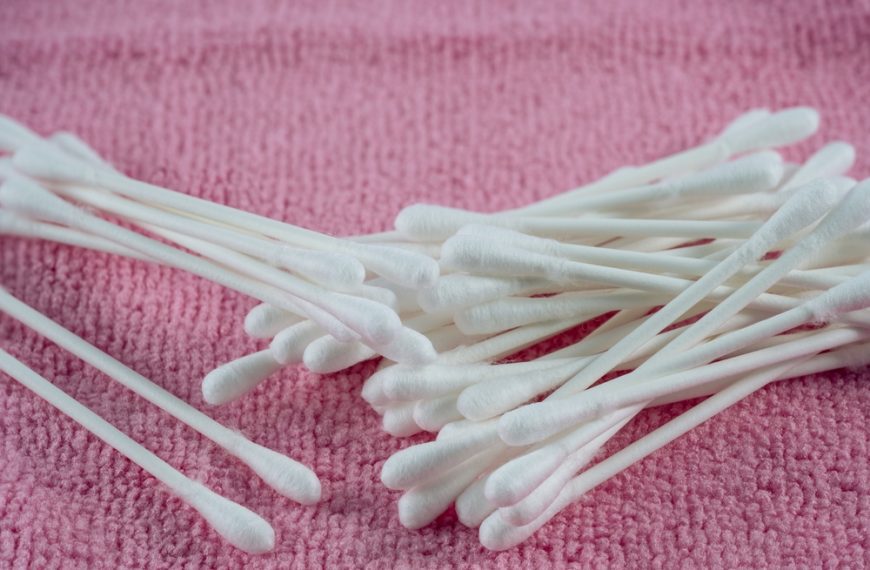Cotton balls and swabs, white fluffy spheres and dual-tipped sticks, paper or plastic stems, arranged in clear jar or plastic packaging, used for hygiene and skincare