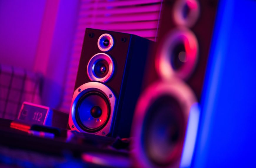 Close-up of black speakers with silver accents, purple and red lighting, blurred background, modern audio setup