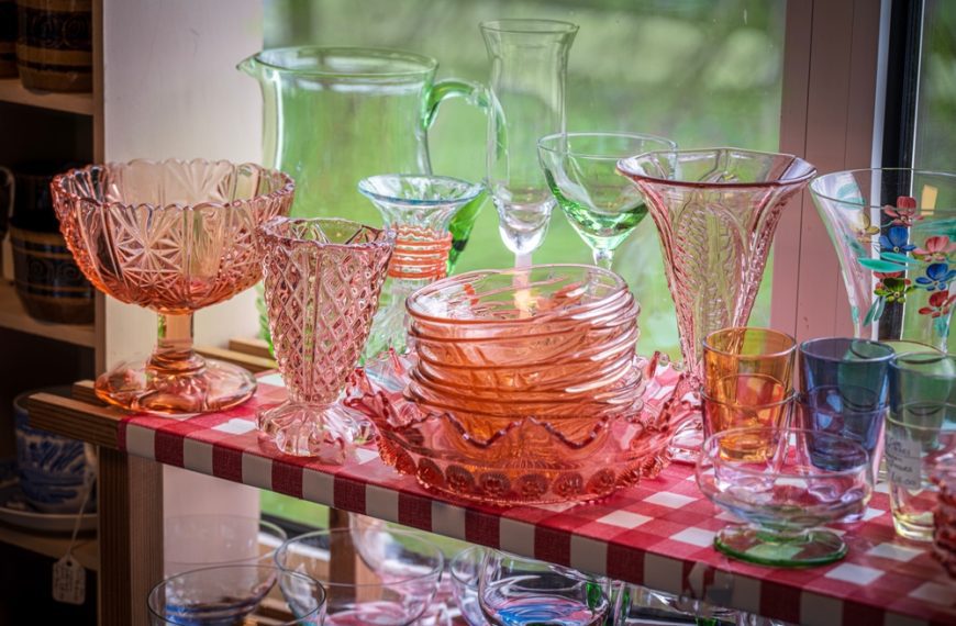 Assorted vintage glassware, pink and green tones, displayed on red-checkered shelf, mix of bowls, vases, pitchers