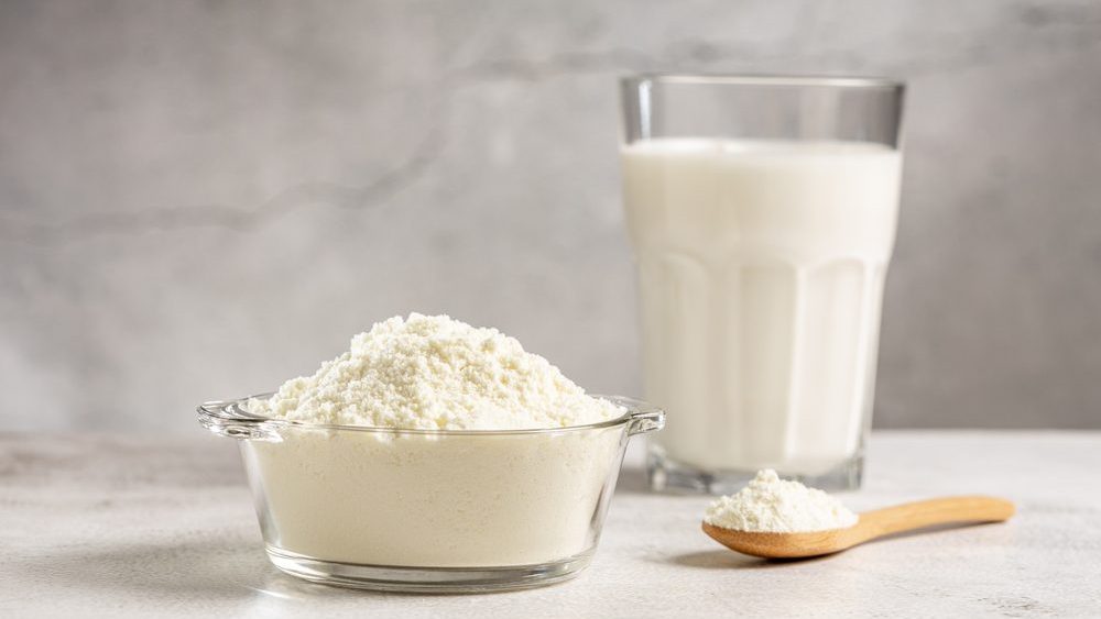 Powdered milk in a glass bowl with a wooden spoon and a glass of reconstituted milk
