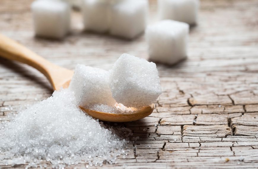 White sugar cubes on a rustic wooden surface, wooden spoon holding a sugar cube, scattered granulated sugar, sweetener concept, traditional sweetening method