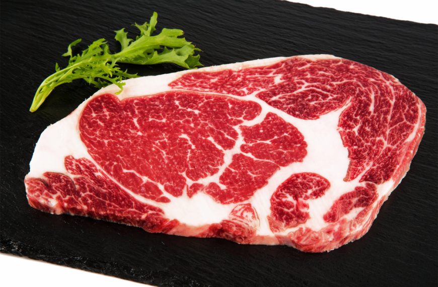 Raw ribeye steak with rich marbling, placed on a black slate surface, high-quality cut for grilling or cooking, fresh and uncooked beef preparation