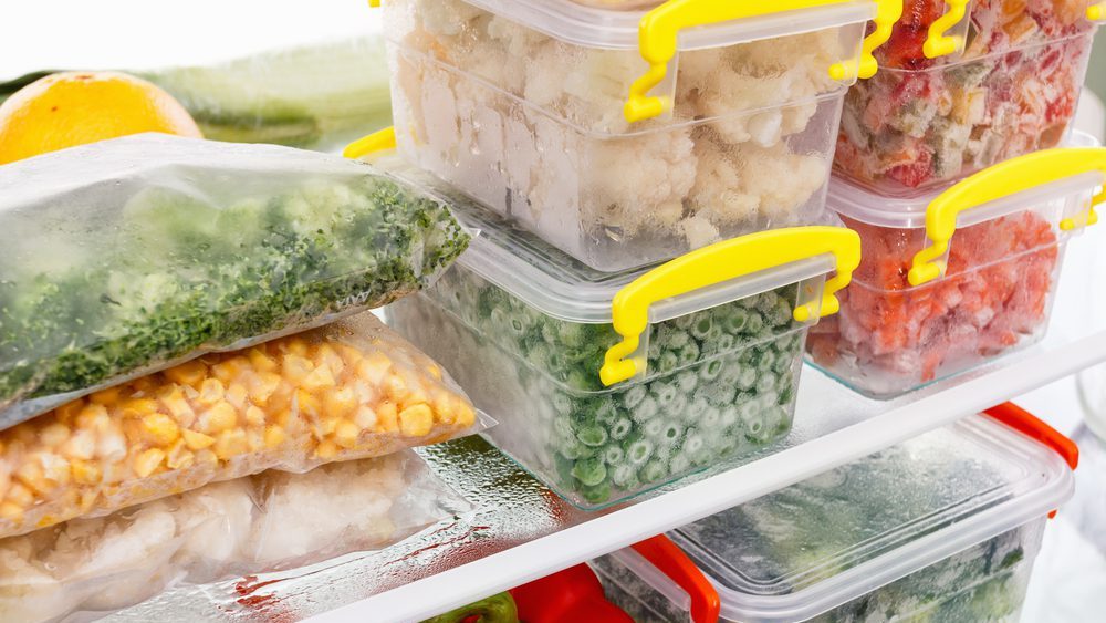 Freezer shelf packed with assorted frozen vegetables, including sealed bags of corn, broccoli, green beans, and bell peppers