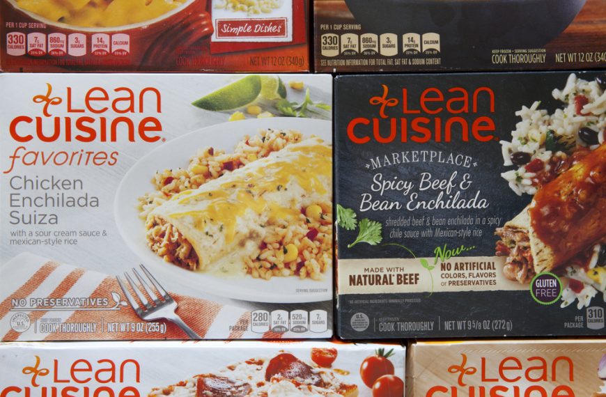 Lean Cuisine frozen meals stacked on shelf, visible flavors include enchiladas and pasta dishes, colorful packaging