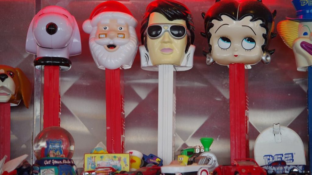 Collection of vintage PEZ dispensers with character heads including Santa, Elvis, Betty Boop, and a robot displayed in case