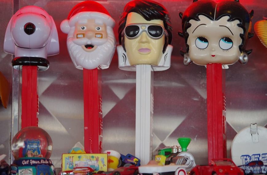 Collection of vintage PEZ dispensers with character heads including Santa, Elvis, Betty Boop, and a robot displayed in case