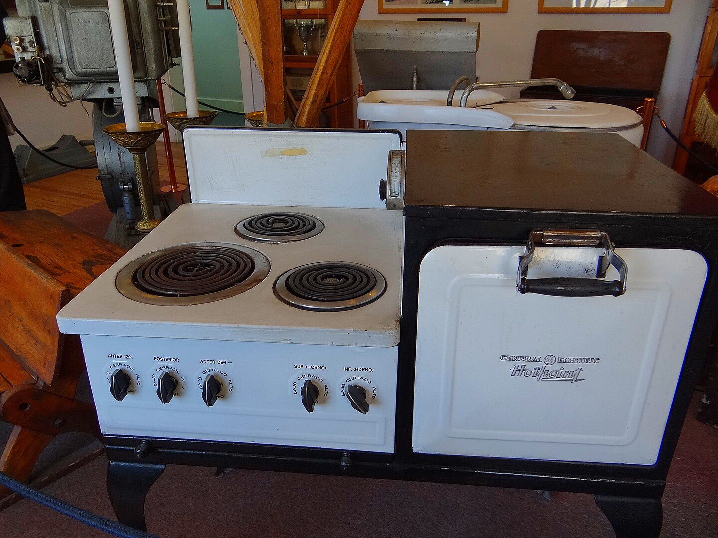 Vintage white General Electric Thriftpoint electric stove with three burners, control knobs, and side oven compartment, displayed in what appears to be a museum or historical setting