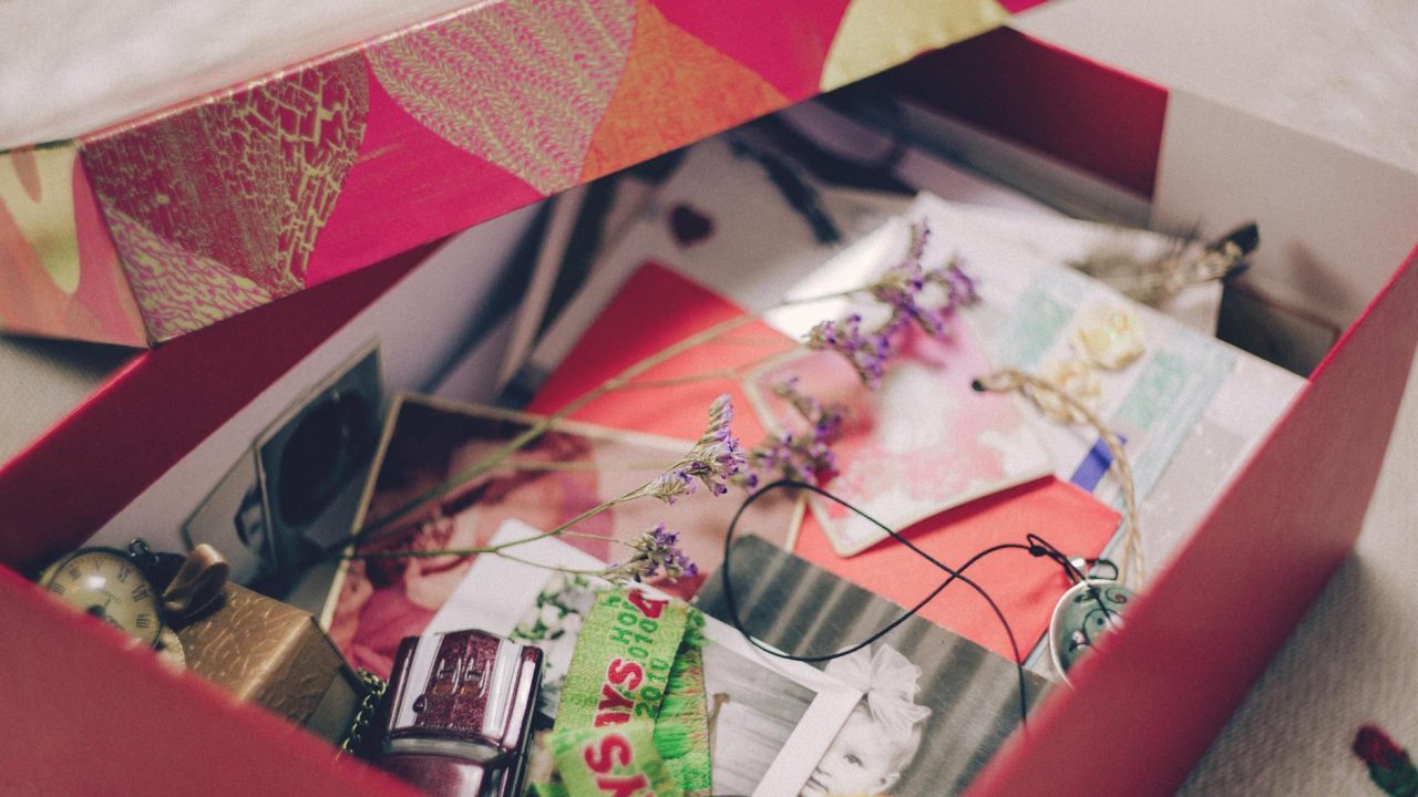 Open box filled with assorted keepsakes, including photos, dried flowers, trinkets, and small personal items