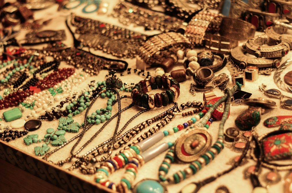 Assorted handmade jewelry on display, various beaded necklaces, bracelets, and rings, earthy tones and vibrant colors, arranged on a flat surface