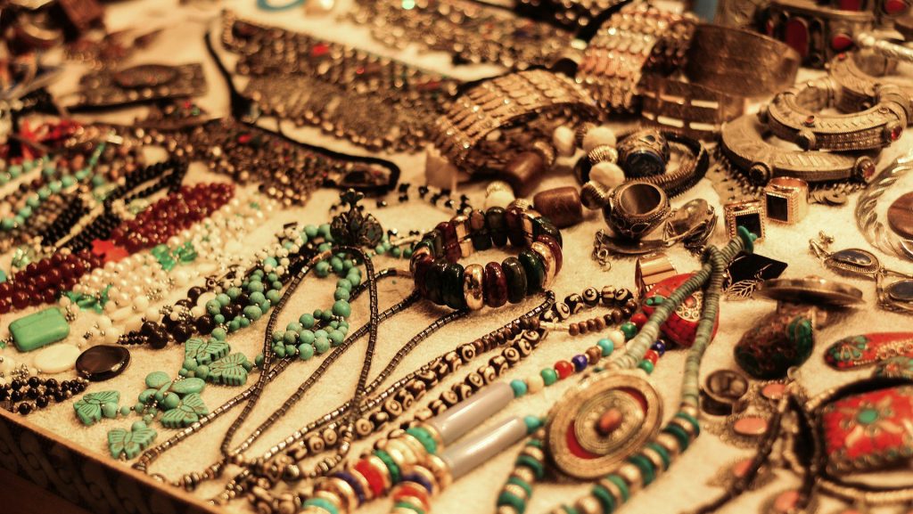Assorted handmade jewelry on display, various beaded necklaces, bracelets, and rings, earthy tones and vibrant colors, arranged on a flat surface