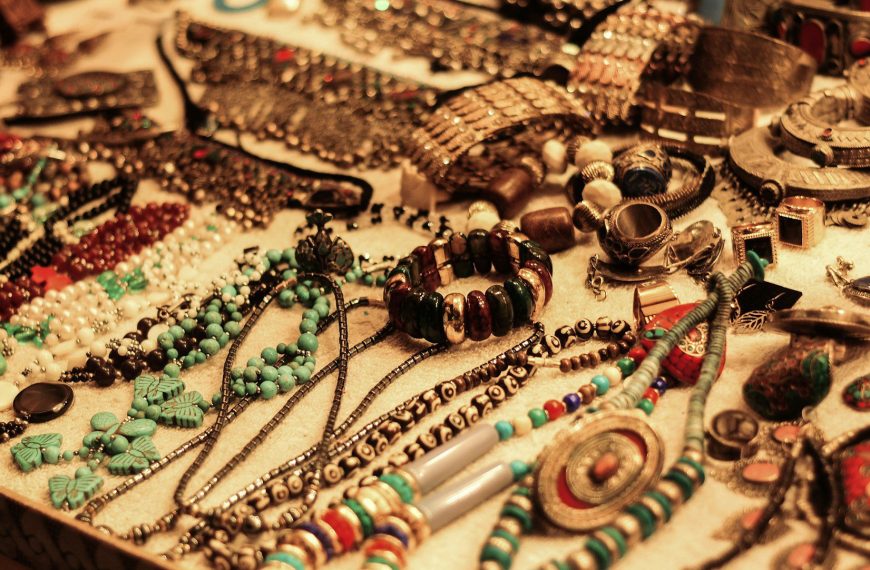 Assorted handmade jewelry on display, various beaded necklaces, bracelets, and rings, earthy tones and vibrant colors, arranged on a flat surface