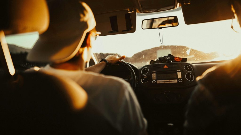 Carpooling, Person wearing a cap driving a car during golden hour, dashboard and windshield illuminated by warm sunlight