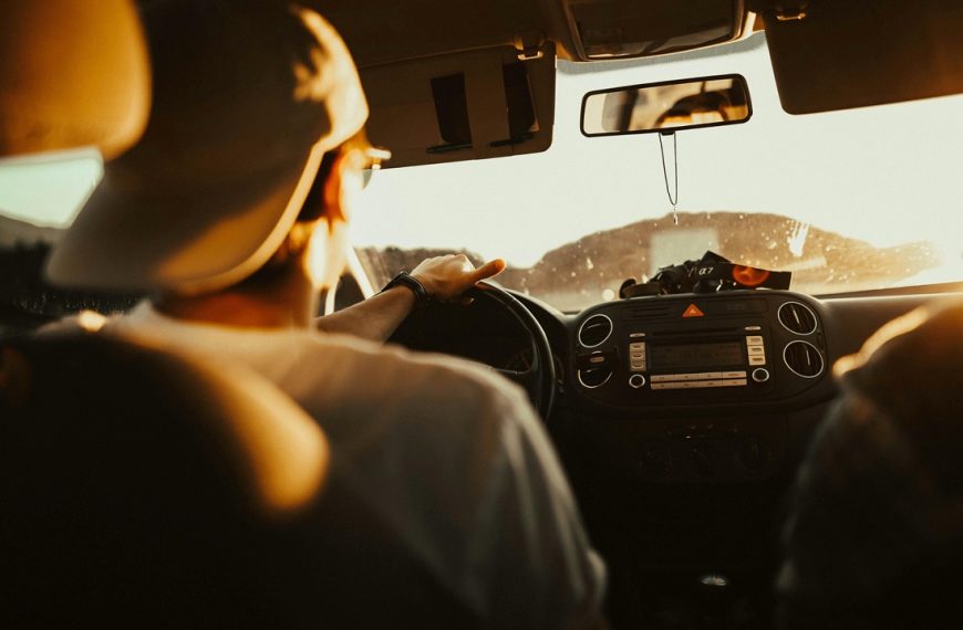 Carpooling, Person wearing a cap driving a car during golden hour, dashboard and windshield illuminated by warm sunlight