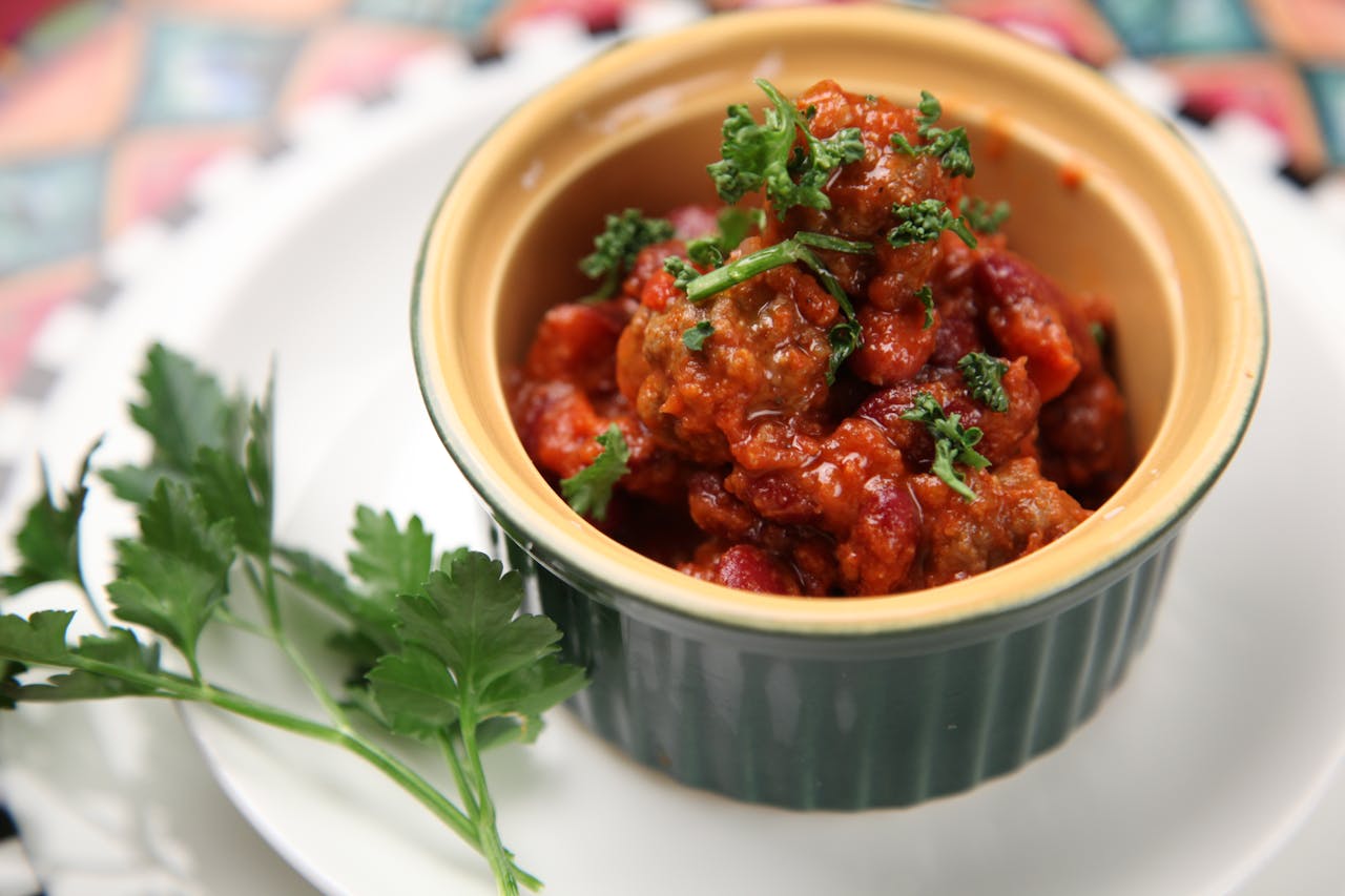 Bowl of chili sin carne with beans, tomato sauce, chopped herbs, served in a green ramekin, garnished with parsley