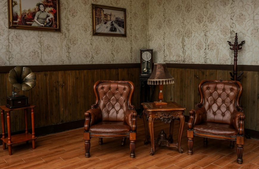 Vintage-style sitting room, two tufted leather armchairs, wooden side table with antique decor, retro wallpaper and wood paneling