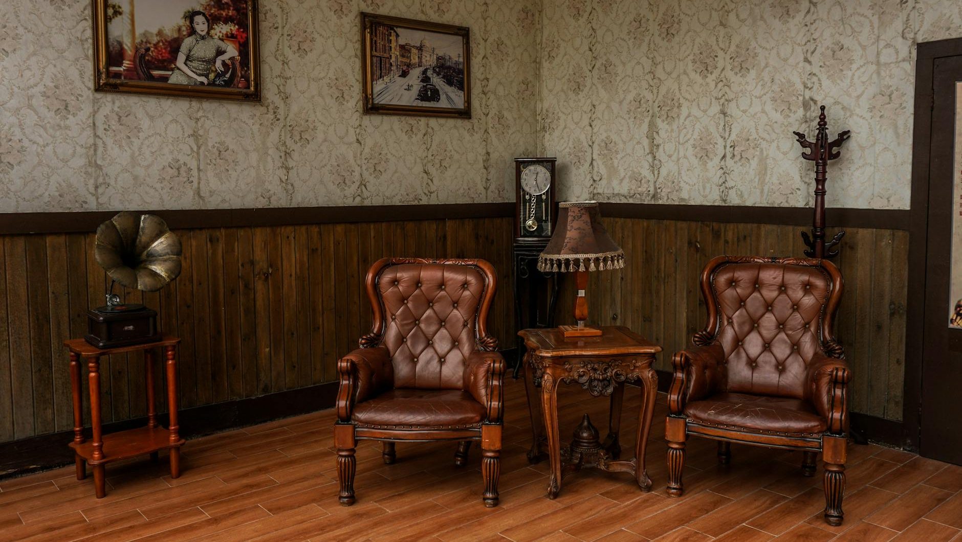 Vintage-style sitting room, two tufted leather armchairs, wooden side table with antique decor, retro wallpaper and wood paneling