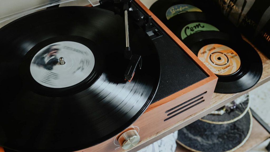 vintage record player spinning a black vinyl record, with stacked records visible nearby