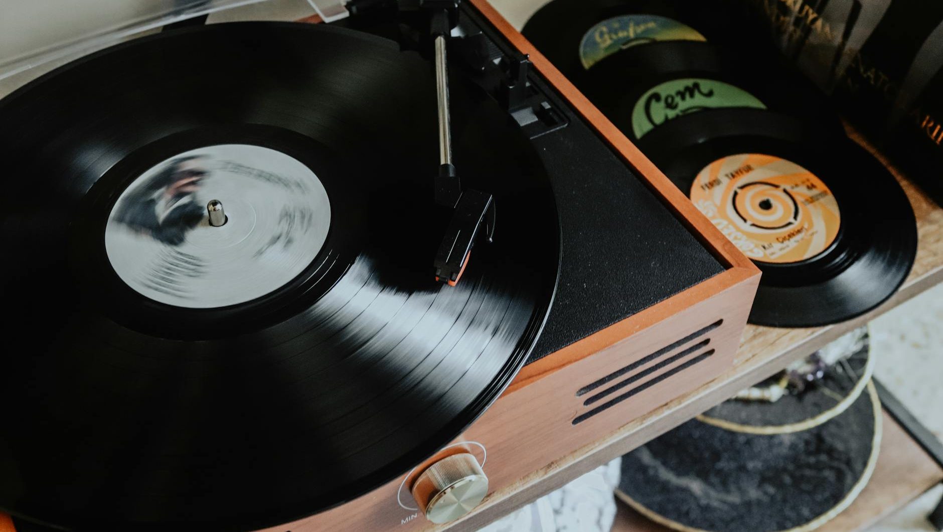 vintage record player spinning a black vinyl record, with stacked records visible nearby