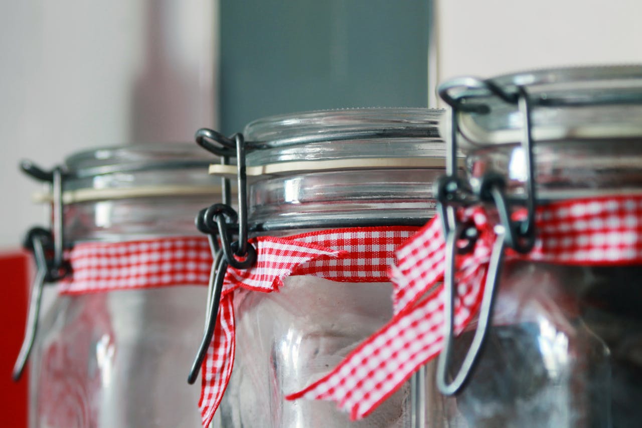 close-up of three glass jars with metal clasps, decorated with red and white gingham ribbons, soft indoor lighting