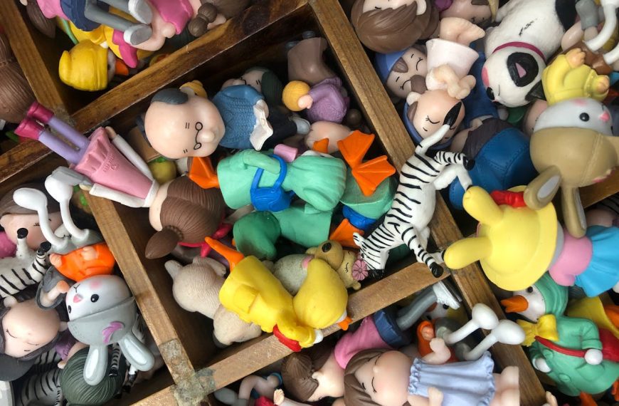 Assorted colorful toy figures, animals, and cartoon characters, scattered in wooden compartments, viewed from above