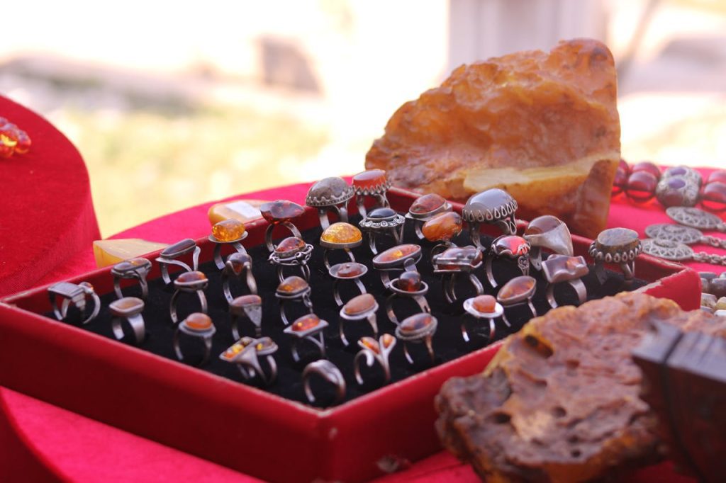 Display of assorted vintage amber rings in a red velvet tray, polished gemstones in silver settings, large amber stones in background