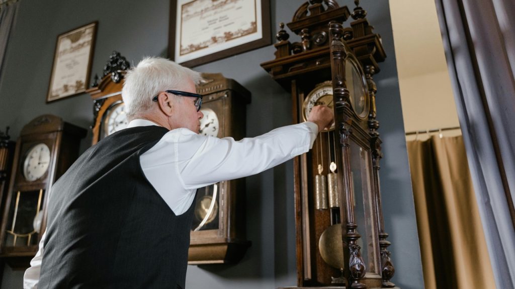 Grandfather clock, Person winding a wooden grandfather clock, ornate gold clock face, visible pendulum, antique design, warm interior lighting