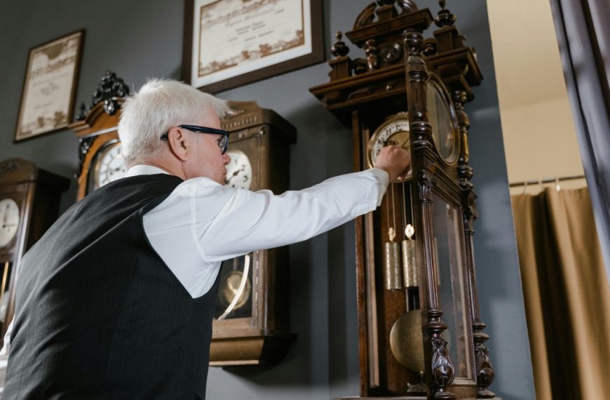 Grandfather clock, Person winding a wooden grandfather clock, ornate gold clock face, visible pendulum, antique design, warm interior lighting