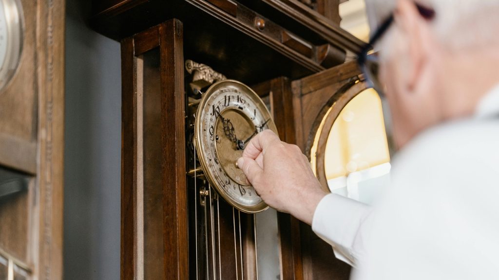 Grandfather clock hands, Person winding a wooden grandfather clock, ornate gold clock face, visible pendulum, antique design, warm interior lighting