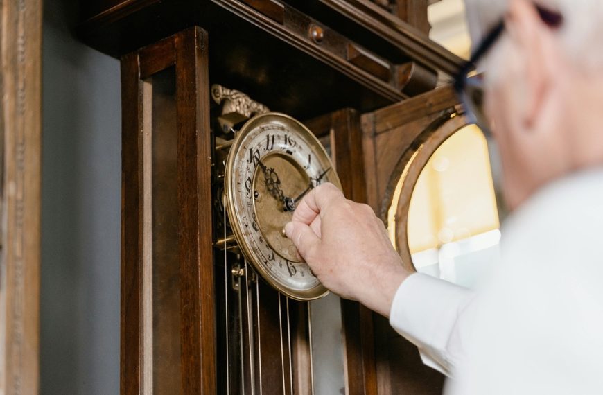 Grandfather clock hands, Person winding a wooden grandfather clock, ornate gold clock face, visible pendulum, antique design, warm interior lighting