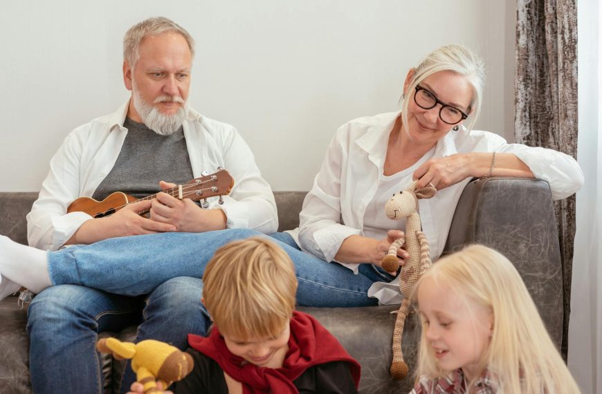 Elderly couple sitting on a couch smiling while two young children play with toys in front of them