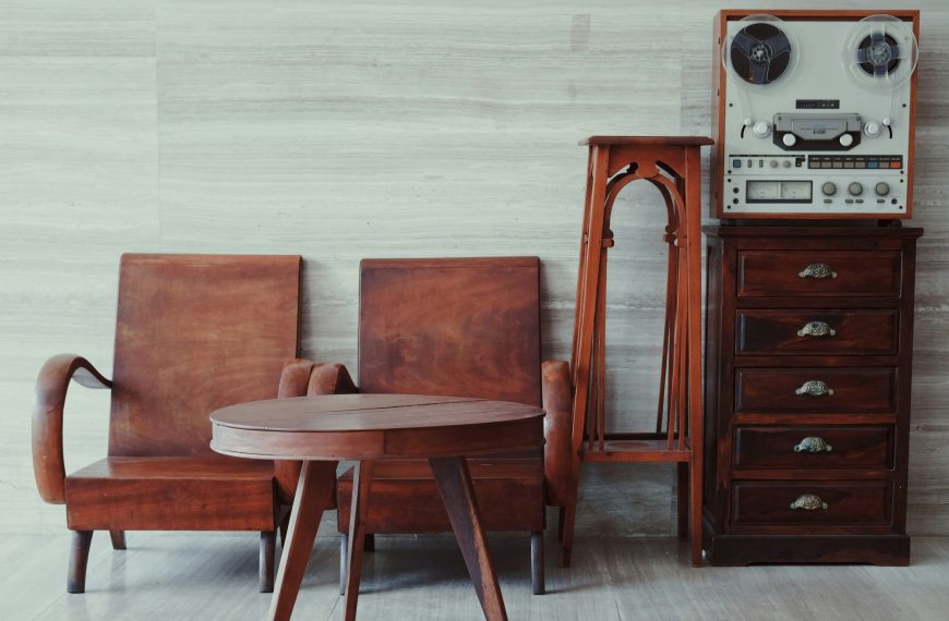 Vintage wooden furniture set, including a mid-century style table, chairs, and a tall chest of drawers, arranged against a neutral-toned wall with tiled flooring