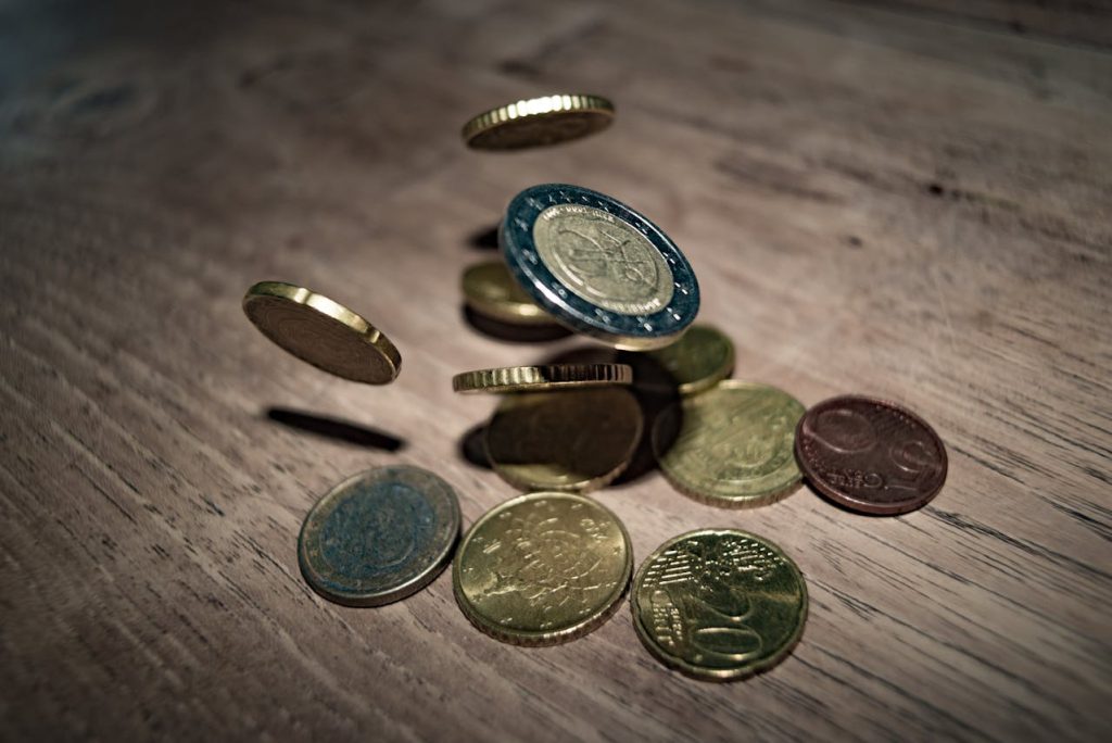 euro coins scattered on wooden table, some coins mid-air, various denominations visible, motion blur, close-up shot