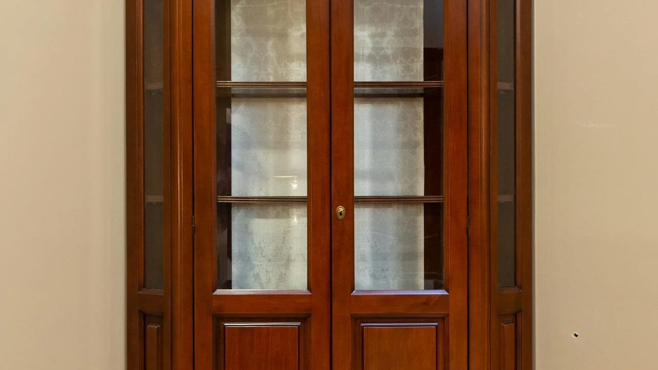 Wooden cabinet with glass-paneled doors, polished brown finish, symmetrical design, vintage style, indoor furniture, standing against a plain beige wall