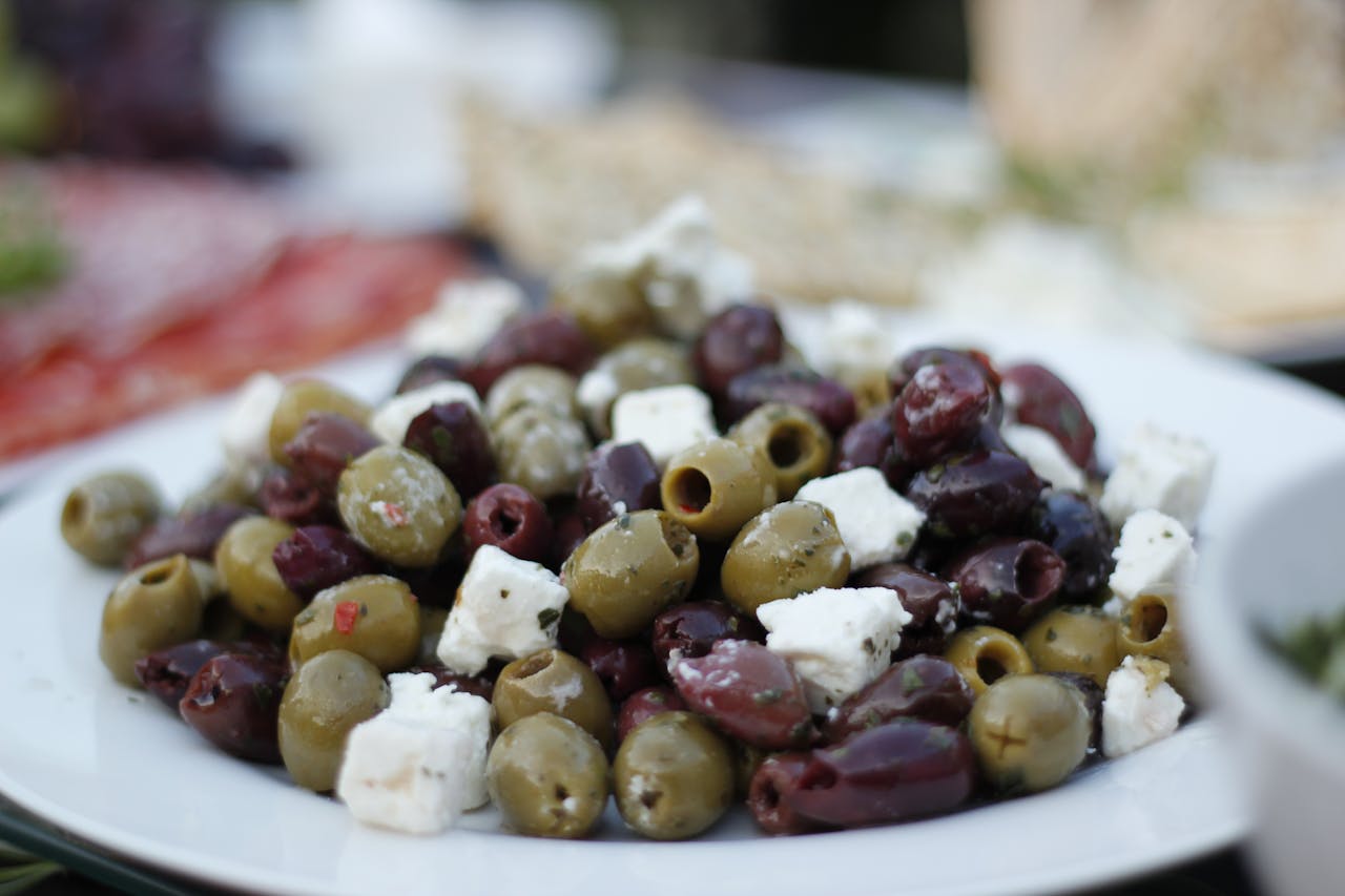Close-up of green and kalamata olives, mixed with cubes of white feta cheese, served on a white plate.