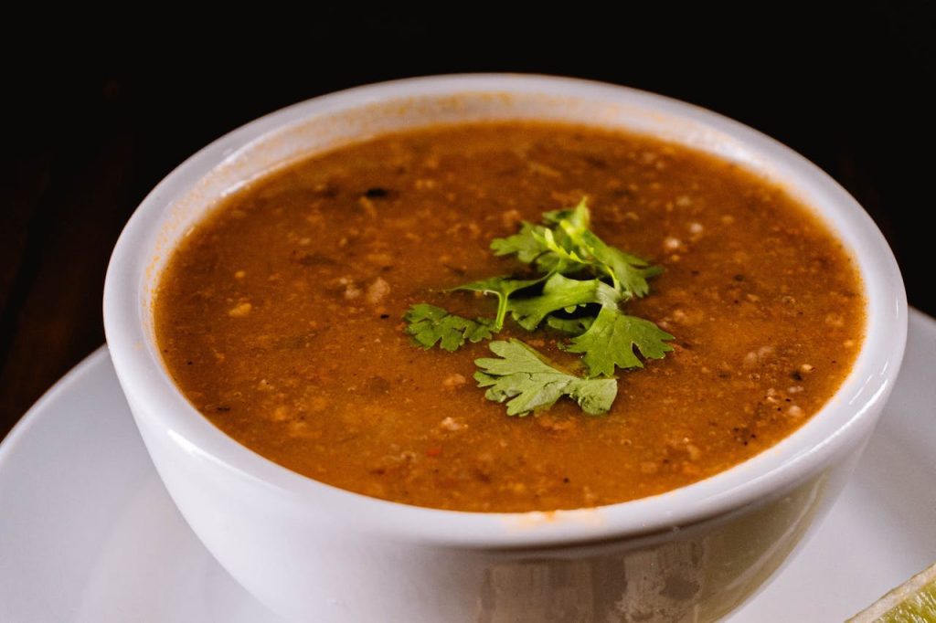 Bowl of lentil soup, garnished with fresh cilantro, served in a white ceramic bowl on a matching saucer