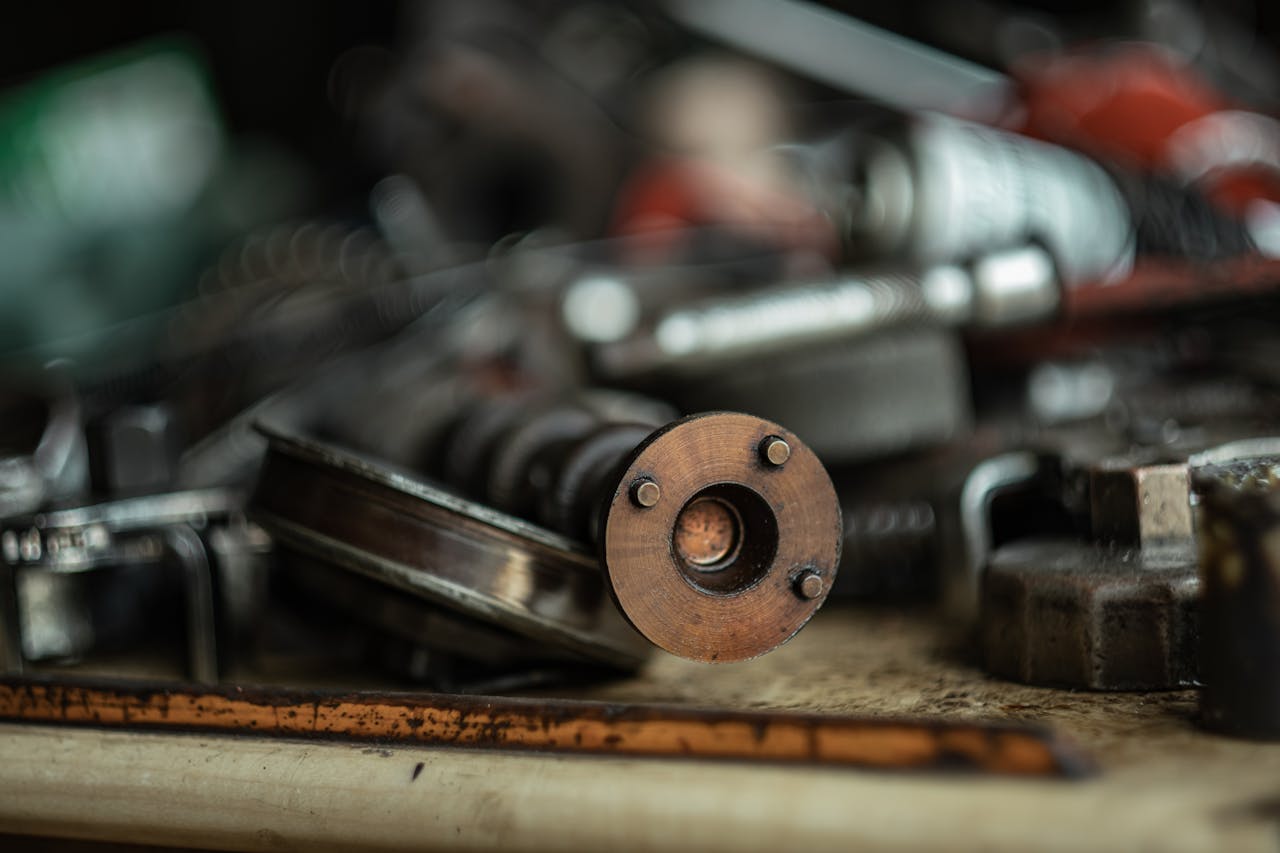 Rusty metal cylinder part, surrounded by various old automotive components, resting on a dusty workbench