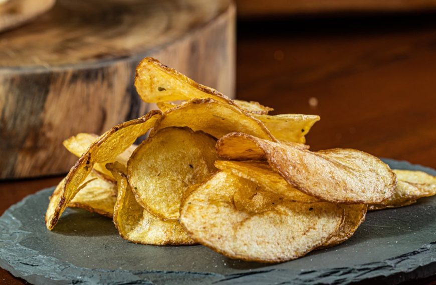 Golden crispy potato chips, slightly curled edges, served on a dark slate plate, rustic wooden background