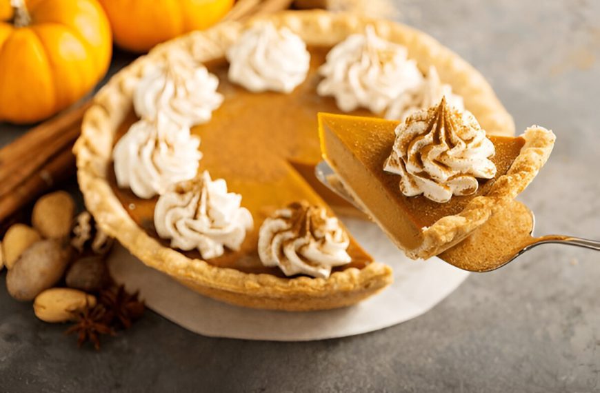 Sweet pumpkin pie decorated with whipped cream and cinnamon with a slice taken out