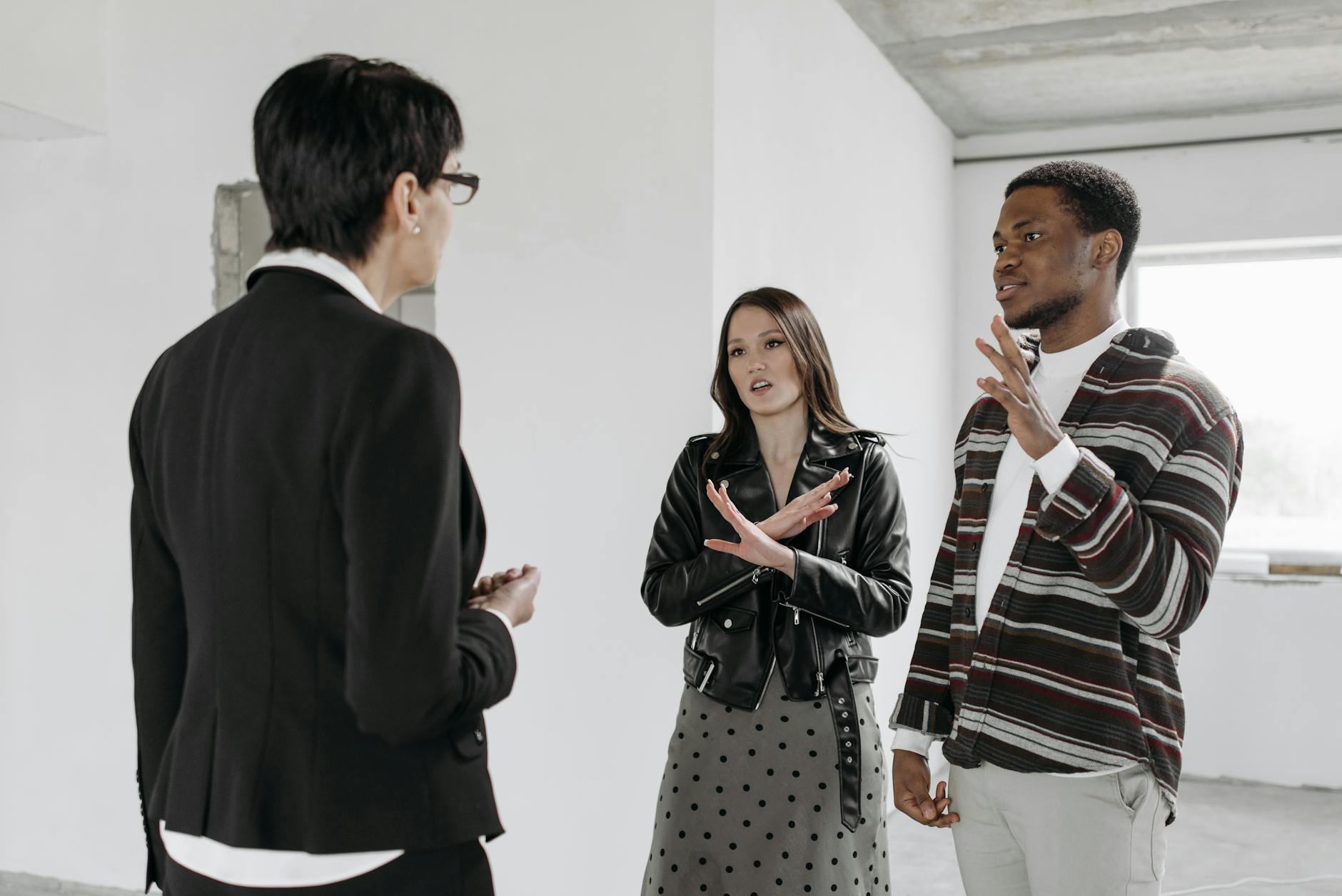 Real estate agent showing a property to a couple in an unfinished room, all three engaged in conversation