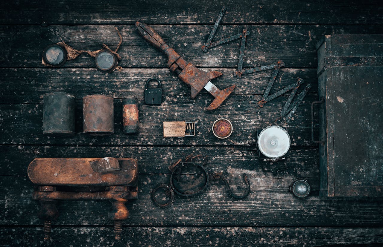 Rusty vintage hand tools and metal items, wooden vise, arranged on a weathered wooden surface, showcasing signs of age, corrosion, and wear