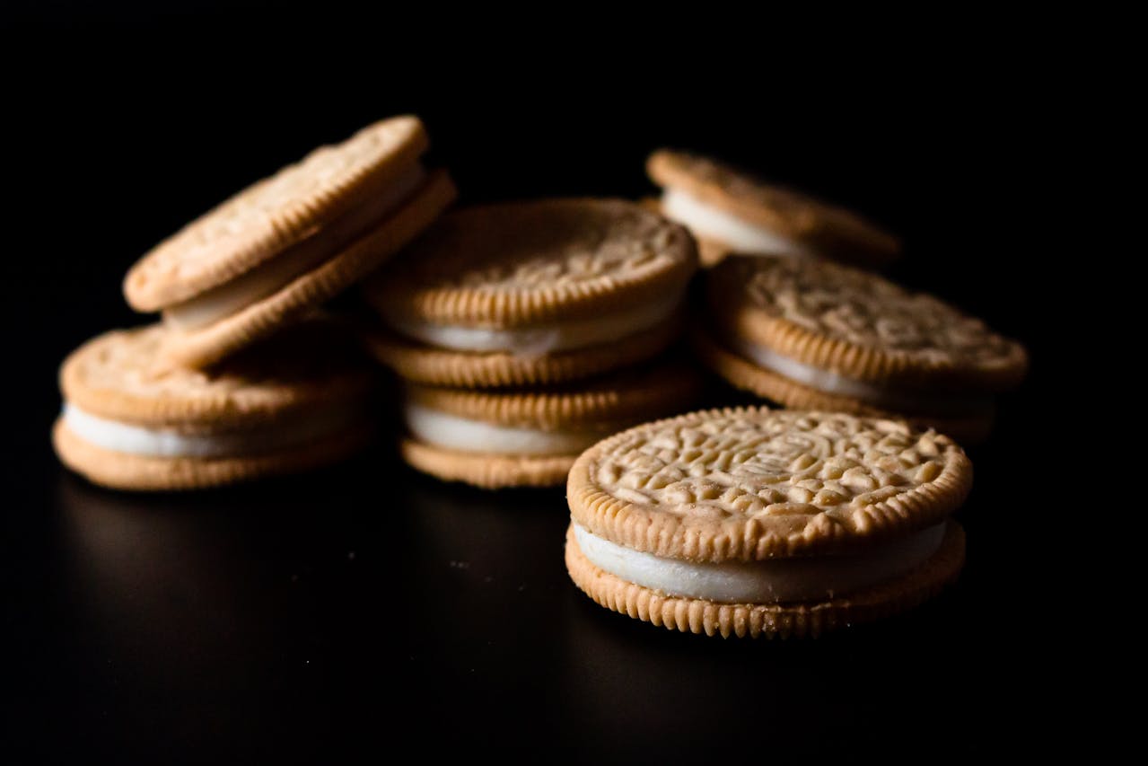 Golden sandwich cookies with cream filling, arranged on a dark surface, close-up shot with shallow depth of field