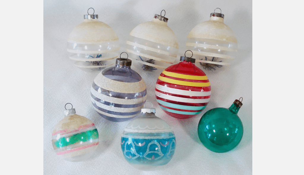 Collection of vintage glass Christmas ornaments in various colors and striped patterns, arranged on a white fabric surface