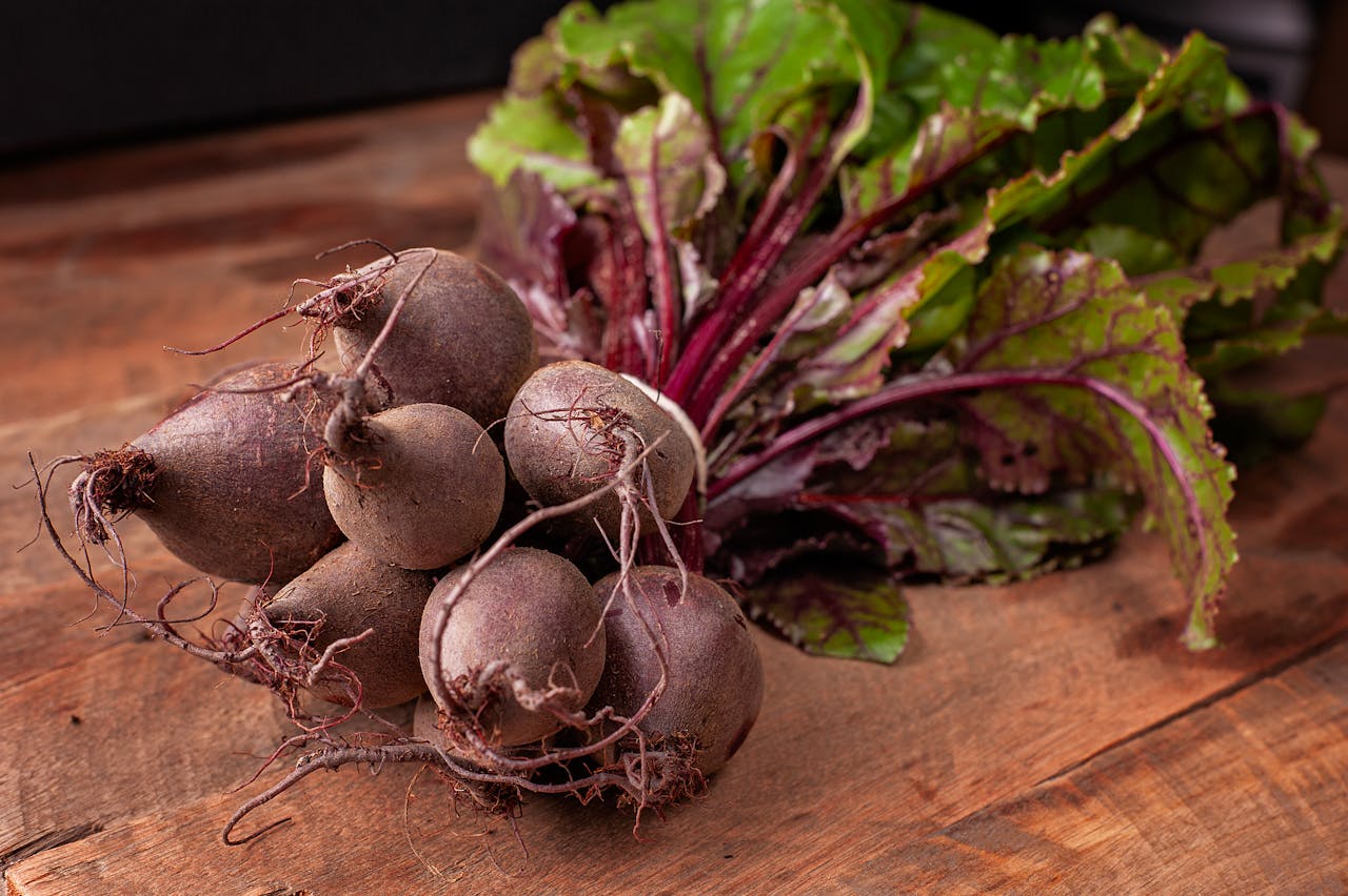Fresh bundle of beets with leafy greens attached, placed on wooden surface, vibrant purple stems and earthy roots visible