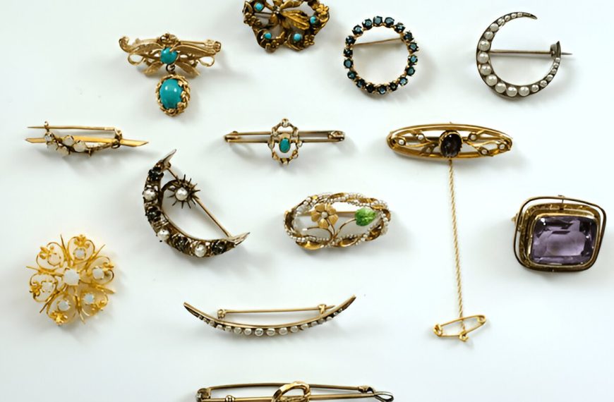 Collection of antique brooches and pins, various shapes and styles, featuring gold, gemstones, pearls, and intricate metalwork, arranged on a white background